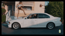 a woman is standing on the steps of a white car with a carton of lychee juice in the background