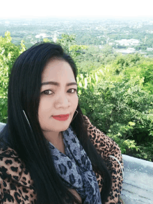 a woman in a leopard print top and scarf stands in front of trees