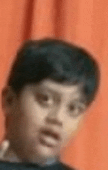 a close up of a young boy making a funny face against an orange curtain .