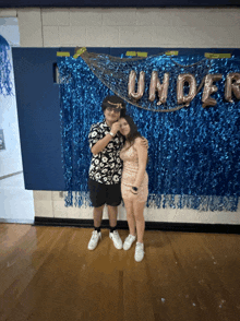 a boy and a girl pose for a picture in front of a banner that says under