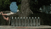 a man with a cartoon face on his head is sitting at a table with a row of water bottles