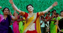 a woman in a red and yellow saree is dancing in front of a crowd of people .