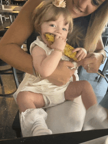 a woman holds a baby who is eating a corn on the cob