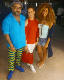 a man in a blue shirt and yellow pants poses for a photo with two women