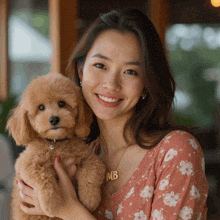 a woman is holding a small brown poodle with a necklace that says mb