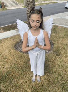 a young girl dressed as an angel with her eyes closed and her hands folded