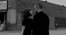 a black and white photo of a man and woman kissing in front of a building that says share loans .