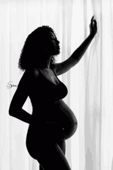 a silhouette of a pregnant woman standing in front of white curtains