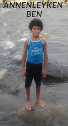 a young boy in a blue tank top stands on a rock near a river with the name anneleyken ben written above him