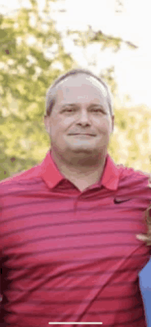 a man in a red and black striped shirt is standing in front of trees .