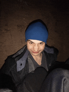 a young man wearing a blue beanie and a black jacket is smiling