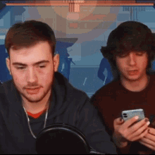 two young men are looking at their phones in front of a sign that says ' a ' on it