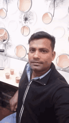 a man in a black jacket is taking a selfie in front of a wall with circles on it