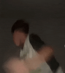 a blurry picture of a man in a white shirt standing in a dark room .