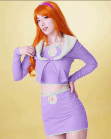 a woman with red hair is wearing a purple top and green skirt