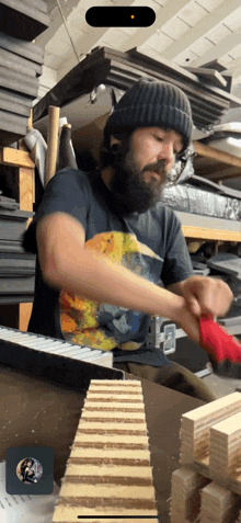 a man with a beard wearing a black shirt with a picture of a cat on it is working on a piece of wood