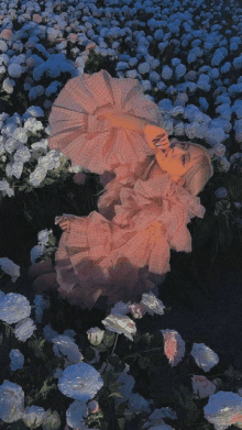 a girl in a pink dress is laying in a field of white flowers