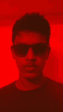 a man wearing sunglasses is standing in front of a red background .