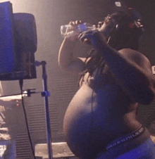 a very fat man is drinking water from a bottle while standing on a stage .