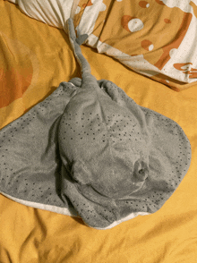 a stuffed stingray is laying on a bed with a yellow blanket