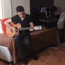 a man sits on a bed playing an acoustic guitar in front of a laptop that says ' dirty '