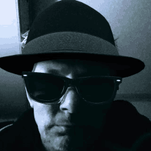 a man wearing a fedora and sunglasses looks at the camera