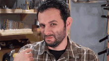 a man with a beard wearing a plaid shirt is standing in front of a shelf full of tools .