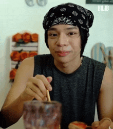 a young man wearing a bandana and a beanie is sitting at a table eating food with a straw .