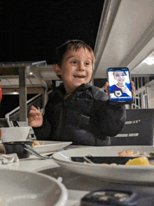 a young boy holds up a cell phone with a picture of a child on the screen