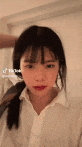 a girl with long hair and bangs is wearing a white shirt and a ponytail .