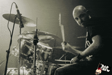 a man playing drums in front of a microphone with a bad crew logo on the bottom