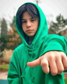 a young man wearing a green hoodie is pointing at the camera .