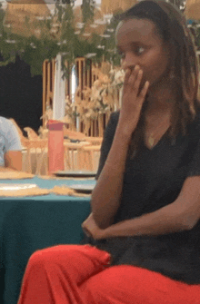 a woman in a black shirt and red pants sits at a table