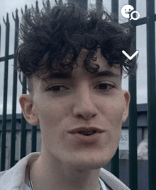 a young man with curly hair is standing in front of a fence and a sign that says s & s