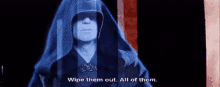 a man in a hooded robe is standing in front of a screen and talking .