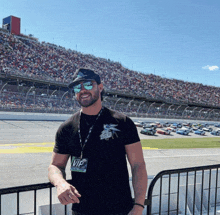 a man wearing sunglasses and a vip tag stands in front of a crowded stadium