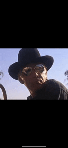 a man wearing a black cowboy hat and sunglasses is looking at the camera .