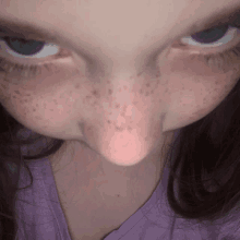 a close up of a girl 's face with freckles and a purple shirt