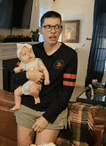 a man in glasses is holding a baby in his arms in a living room .