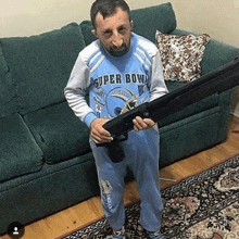 a man in a blue shirt is holding a shotgun in a living room .