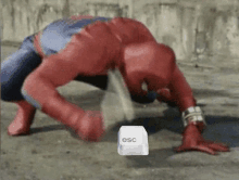 a spiderman is crawling on the ground next to an esc key .