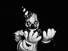 a black and white photo of a scary clown holding something in his hands .