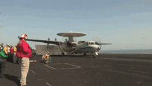 a man in a red jacket stands in front of a plane that says ' us navy ' on the side