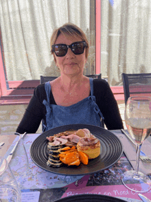 a woman wearing sunglasses sits at a table with a plate of food