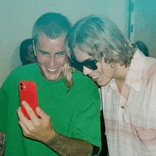 a man in a green shirt is taking a selfie with another man in sunglasses .