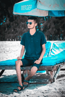 a man wearing sunglasses sits on a beach under an umbrella that says berger