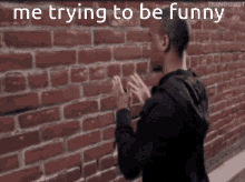 a man standing in front of a brick wall with the words " me trying to be funny " on the bottom