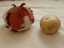 a stuffed animal with red hair sits next to a small potato