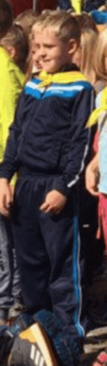 a boy in a blue and yellow tracksuit is standing in a crowd