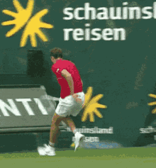 a man in a red shirt and white shorts is running on a tennis court in front of a sign that says schauins reisen